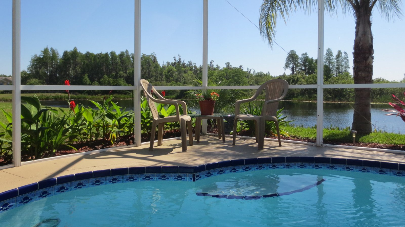 Screened pool enclosure with two chairs beside the pool, overlooking a lake in Florida