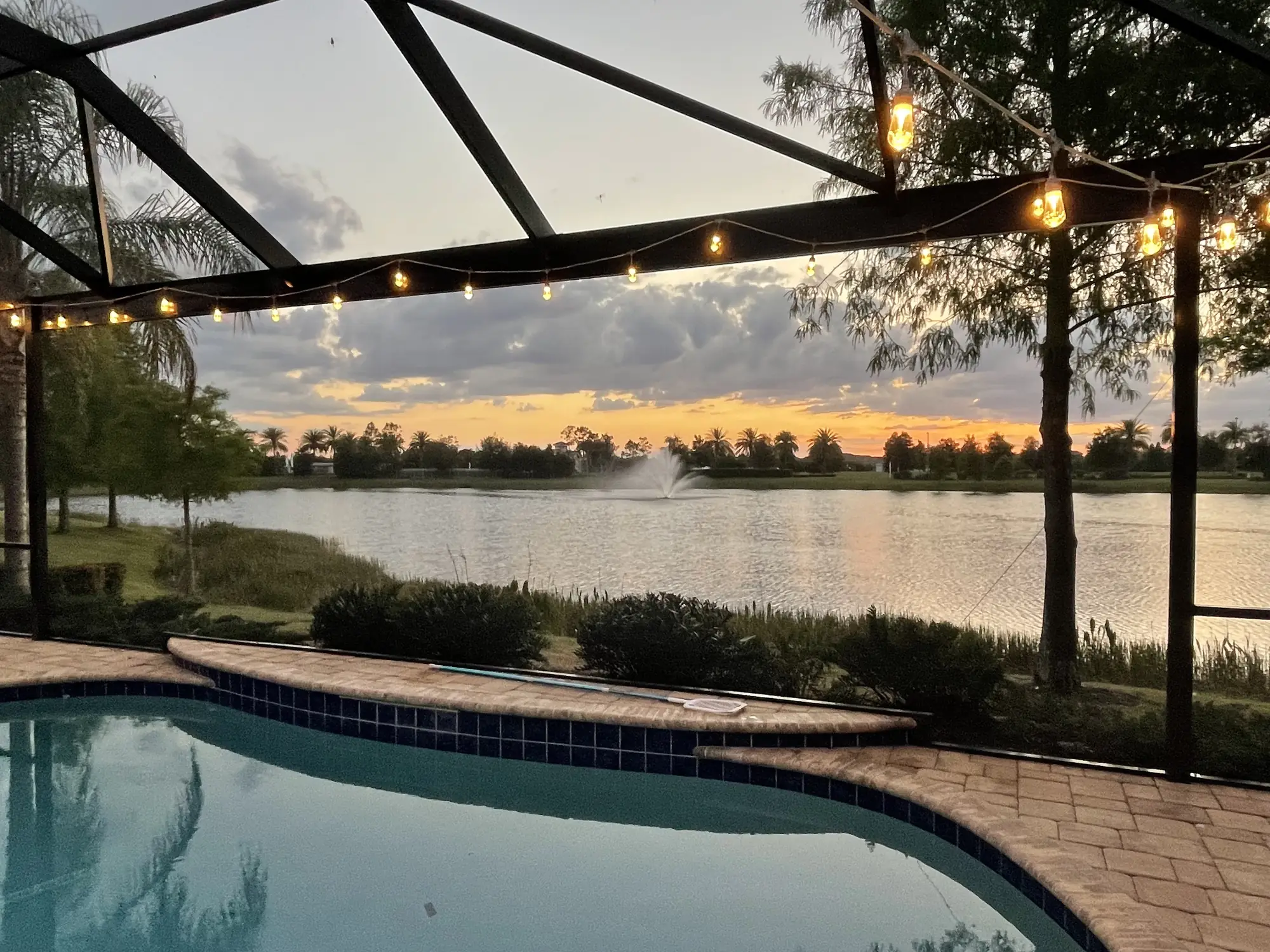 Sunset over a lake seen through a screened pool cage with string lights in Sarasota County