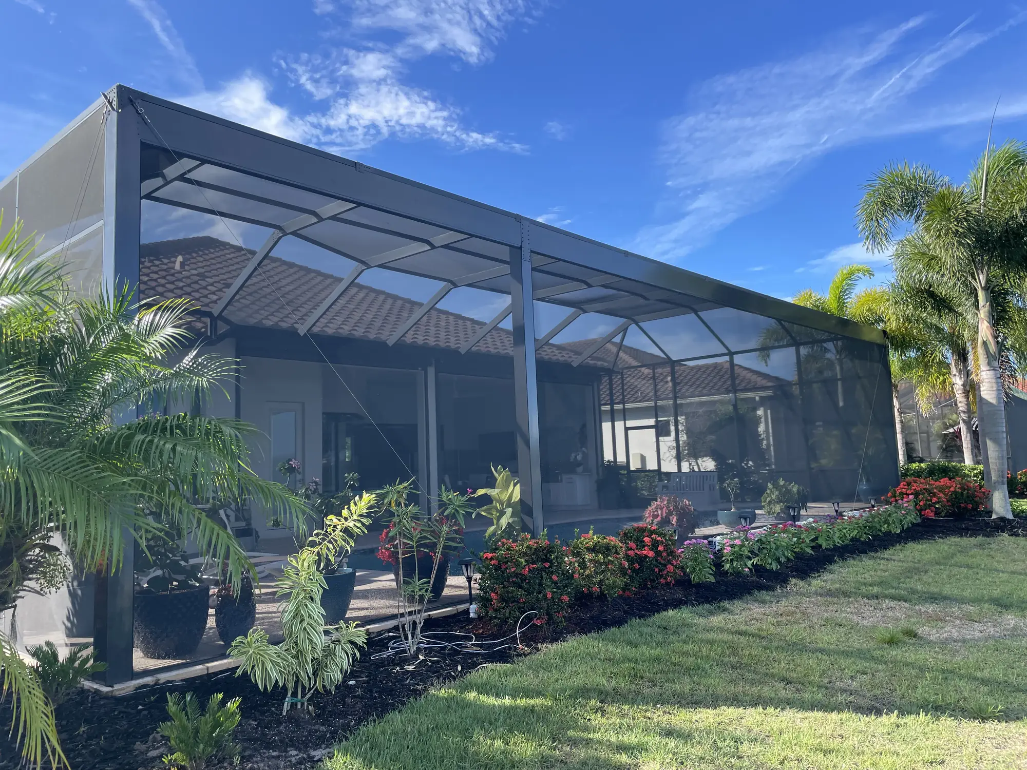 Large bronze aluminum pool cage seen from outside a Florida home surrounded by palms