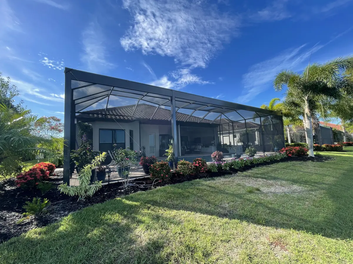 Bronze aluminum pool cage seen from the yard of a Florida home with palm trees and blue sky