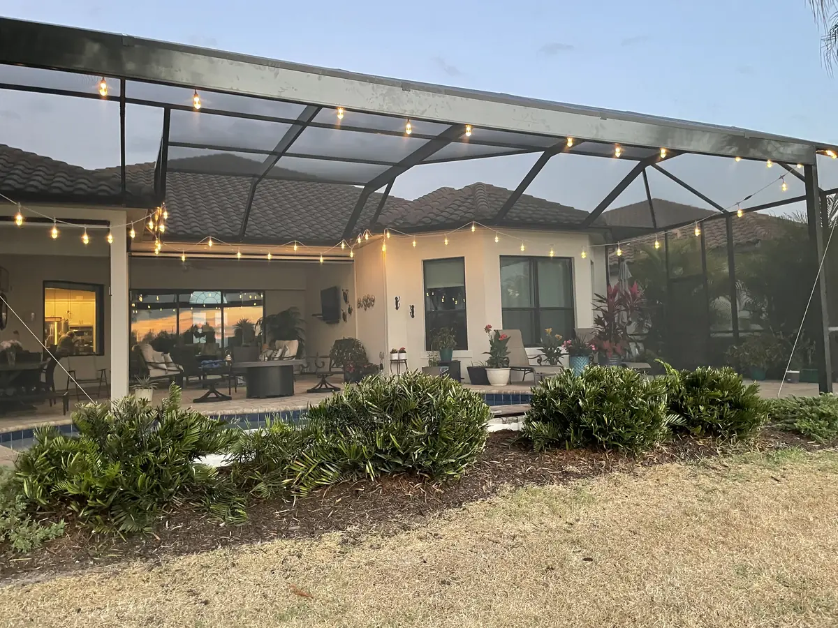 Screened lanai enclosure lit with string lights at dusk behind a Florida home