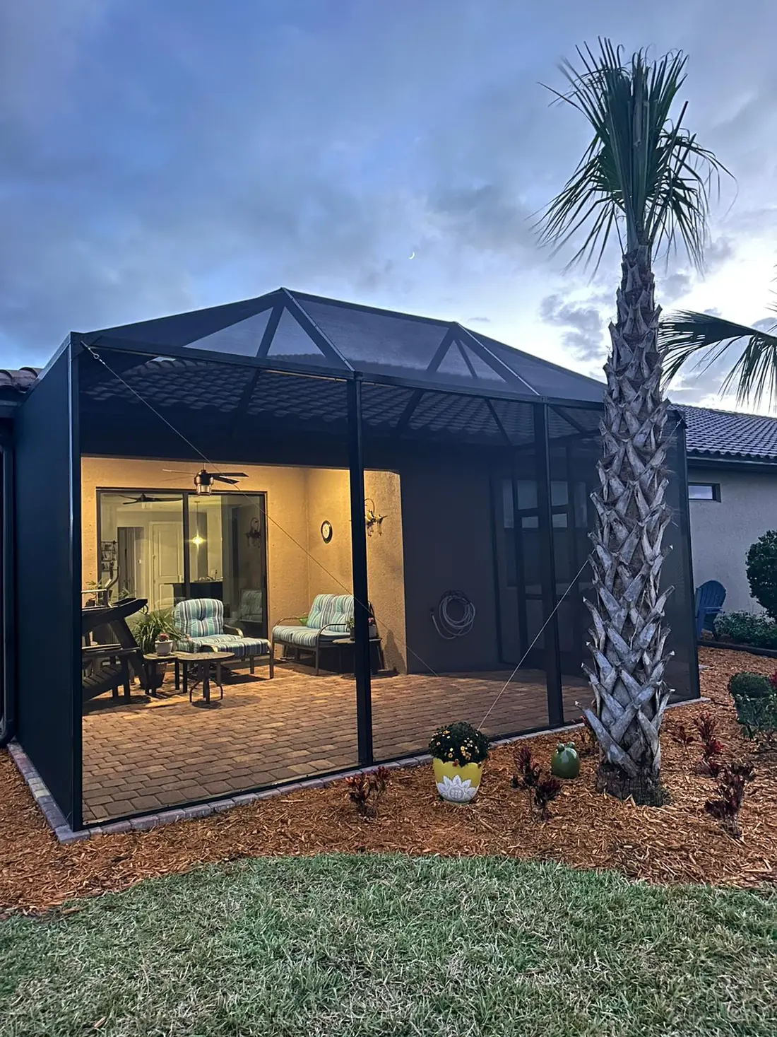 Screened lanai enclosure with warm interior lighting seen from the yard in the evening
